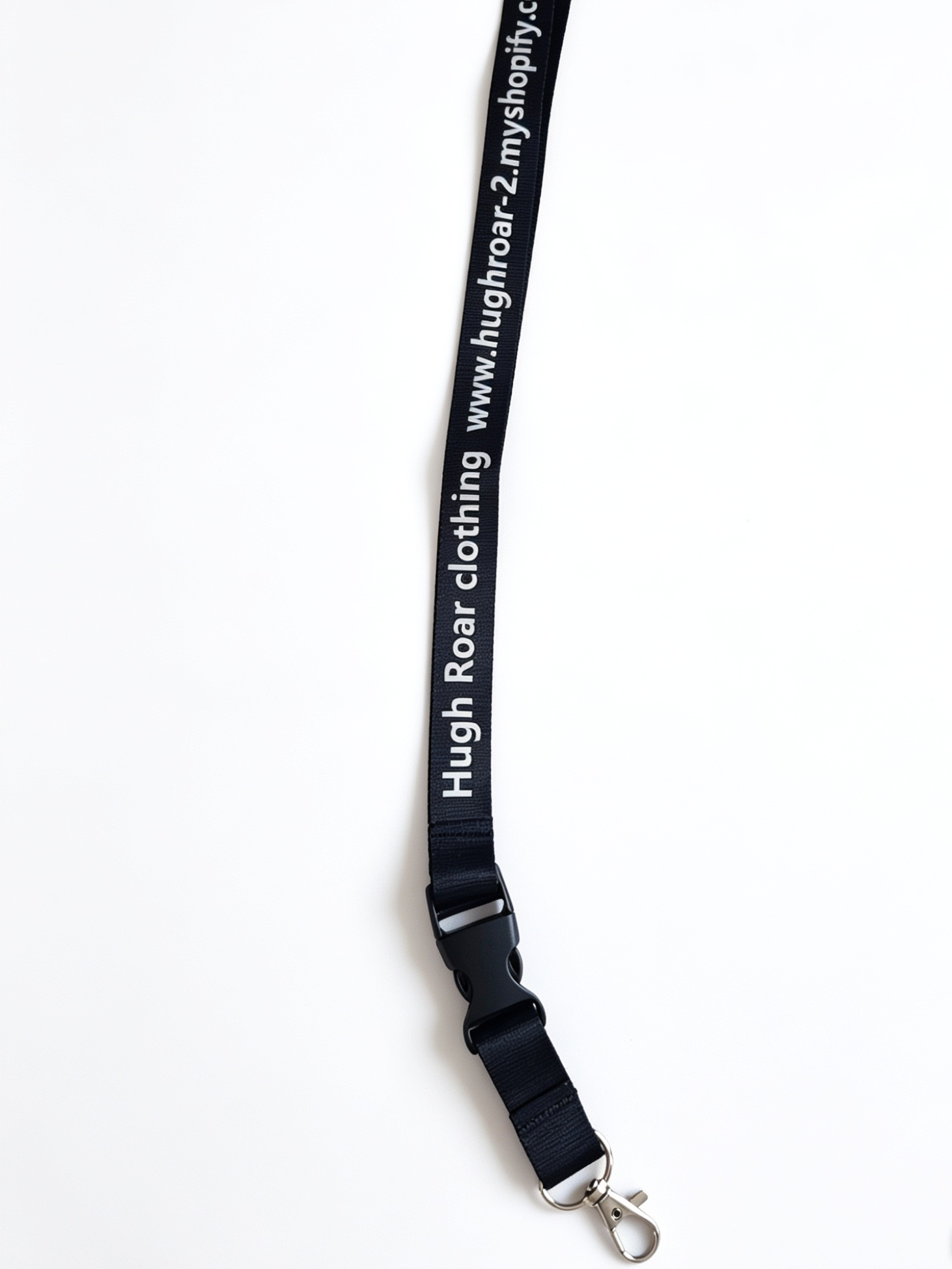 A black fabric strap with white printed text reading 'Hugh Roar clothing' and a website URL, attached to a silver metal lobster clasp.